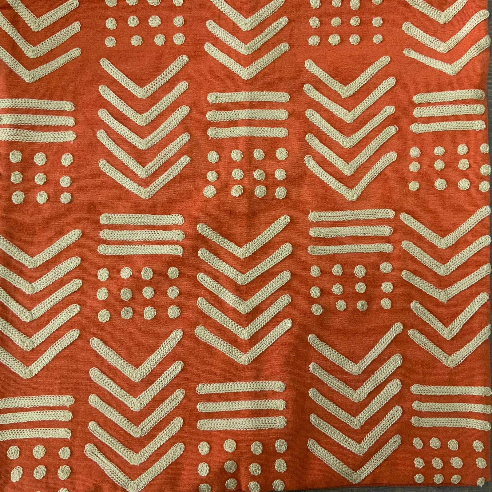 Square terracotta orange throw pillow cover with raised gold-toned geometric embroidery in a tribal mudcloth design featuring chevrons and dots.